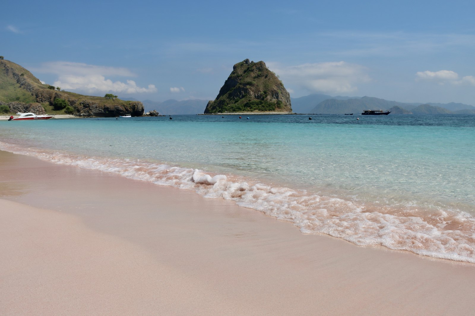 Pink beach with clear water under a blue sky.